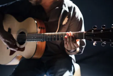 Ein Musiker spielt Gitarre in einem dunklen Raum. Die Hände greifen die Saiten und erzeugen Musik.