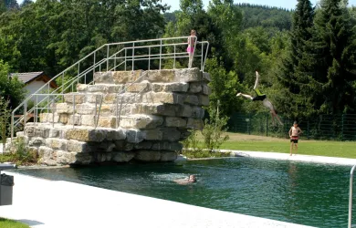 Ein natürlicher Pool mit einer Steinplattform zum Springen. Kinder haben Spaß beim Schwimmen und Springen ins Wasser.