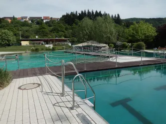 Ein ruhiger Swimmingpool mit Holzterrassen und viel Grün in der Umgebung. Die Wasserflächen sind klar und einladend, ideal für entspannende Tage.