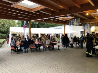 Ein belebtes Fest mit vielen Menschen, die an Tischen sitzen und essen. Zelte im Hintergrund schaffen eine festliche Atmosphäre.