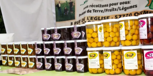 Eine Auslage von verschiedenen eingelegten Früchten und Marmeladen in transparenten Behältern. Die Produkte sind ordentlich angeordnet und zeigen eine Vielfalt an Farben und Geschmäckern.