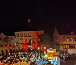 Überblick über das Festgelände bei Nacht. Man sieht eine Menschenmenge auf dem beleuchteten Platz.