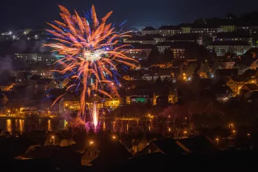 Ein spektakuläres Feuerwerk über einer Stadt bei Nacht. Die bunten Lichter reflektieren sich im Wasser und erhellen die Umgebung.