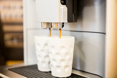 Eine Kaffeemaschine brüht gerade zwei Tassen Kaffee. Die Tassen sind weiß und haben ein modernes, strukturiertes Design.