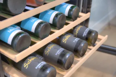 Eine Weinregal mit mehreren Flaschen, die ordentlich aufgereiht sind. Die Etiketten sind in verschiedenen Farben gehalten.