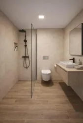 Ein modernes Badezimmer mit einer Glasdusche und hellen Fliesen. Die Einrichtung ist minimalistisch, mit einem Waschbecken und einem WC.