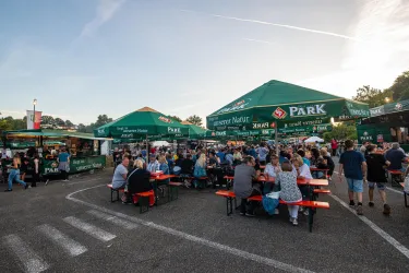Ein belebter Essensmarkt mit mehreren Ständen und großen Zelten. Viele Menschen sitzen an den Tischen und genießen ihre Speisen.