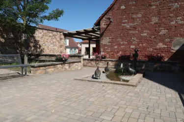 Ein gemütlicher Innenhof mit Steinpflaster und blühenden Pflanzen. Im Mittelpunkt stehen mehrere Skulpturen, umgeben von einem roten Backsteingebäude.