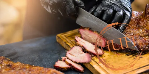 Ein Koch schneidet saftiges, geräuchertes Fleisch auf einem Holzbrett. Die Dunkelheit der Handschuhe und die reichhaltige Textur des Fleisches betonen die Köstlichkeit des Gerichts.