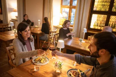Ein gemütliches Restaurant mit Holzstühlen und Tischen. Ein Paar stößt mit Weingläsern an, während andere Gäste ebenfalls speisen.