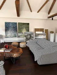 Ein modernes Wohnzimmer mit Holzparkett und hohen Decken. Es gibt ein Bett mit gemusterter Bettwäsche und mehrere Kunstwerke an den Wänden.