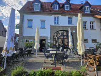 Ein Restaurant mit einer einladenden Terrasse und Sonnenschirmen. Das Gebäude hat eine helle Fassade und große Fenster.