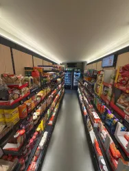 Ein Gang in einem Supermarkt mit Regalen voller Lebensmittel und Snacks. Auf der linken Seite sind verschiedene Produkte und auf der rechten Seite stehen Getränke im Kühlschrank.