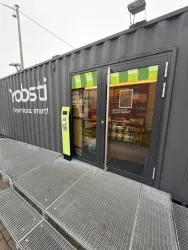 Ein moderner Verkaufscontainer mit großen Fenstern und einem Begrüßungsschild. Vor dem Eingang befindet sich eine kleine Abstellfläche.
