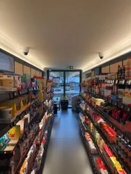 Ein langer Gang in einem Geschäft mit Regalen voller Lebensmittel und Getränken. Am Ende des Gangs ist eine Glastür, die nach draußen führt.