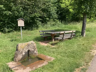 Ein schöner Rastplatz mit einer Bank und einem Tisch aus Holz. Nebenan steht eine Steinsäule mit fließendem Wasser.