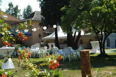Ein schöner Garten mit Tischen und Stühlen für eine Veranstaltung. Im Hintergrund sind Zelte und dekorative Laternen zu sehen.