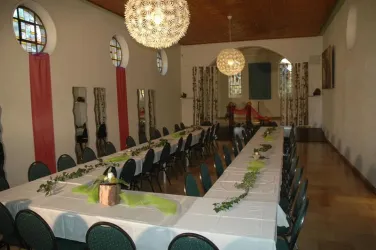 Ein festlich dekorierter Raum mit einem langen Tisch und grünen Akzenten. Die Umgebung ist hell und einladend, ideal für Veranstaltungen.