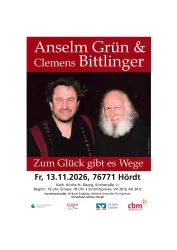 Ein Mann spielt Gitarre und singt in einem Raum mit bunten Fenstern. Es ist eine gemütliche Atmosphäre mit einem Tisch auf der linken Seite.
