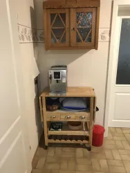 Eine kleine Küchenzeile mit einem Holzschrank und einem Küchenwagen. Auf dem Wagen steht eine Kaffeemaschine und einige Utensilien.