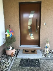 Eine Haustür mit einem modernen Design und einer Glasverzierung. Vor der Tür stehen dekorative Elemente wie Pflanzen und eine bunte Windmühle.