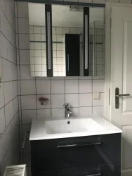 Ein modernes Badezimmer mit einem Waschbecken und einem großen Spiegel. Die Wände sind gefliest und die Beleuchtung ist hell.