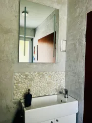 Ein modernes Badezimmer mit einem Waschbecken und einem großen Spiegel. Die Wände sind in einem schlichten Grauton gehalten, und es gibt eine dekorative Steinmosaikfläche.