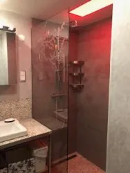 Ein modernes Badezimmer mit einer gläsernen Dusche und stilvollen Wänden. Im Hintergrund ist ein Waschbecken und ein Spiegel zu sehen.