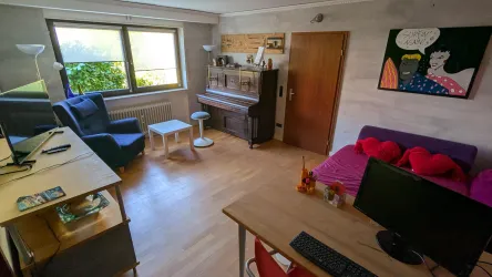 Ein gemütliches Wohnzimmer mit einer blauen Couch und einem Klavier. Der Raum hat viel Tageslicht und eine freundliche Atmosphäre.
