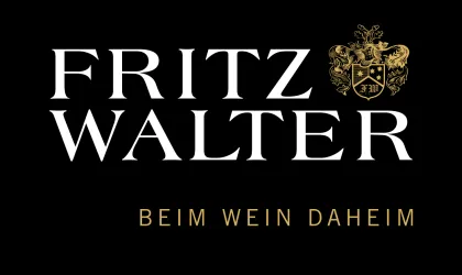 Ein elegantes Logo mit dem Namen "Fritz Walter" in großen, auffälligen Buchstaben. Darunter steht "Beim Wein Daheim", unterstrichen von einem Wappen.