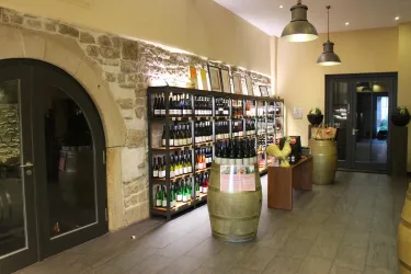 Ein eleganter Weinladen mit Regalen voller Weinflaschen und einem modernen Ambiente. Die Wände sind aus Stein, und im Hintergrund sieht man einen Empfangsbereich.