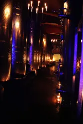 Ein dunkler Gang in einem Weinkeller, beleuchtet von Kerzen und sanften blauen Lichtern. Die Wände sind mit großen, glänzenden Metallbehältern ausgestattet.