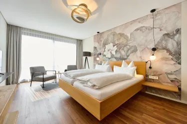 Ein modernes Hotelzimmer mit einem großen Bett und dekorativen Kissen. Die Wände sind mit sanften Farben gestaltet, und ein Fenster sorgt für viel natürliches Licht.