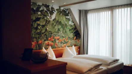 Ein gemütliches Schlafzimmer mit zwei Betten und einer Fototapete von Blumen. Große Fenster lassen viel natürliches Licht herein.