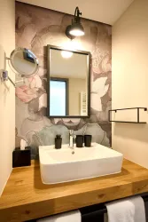 Ein modernes Badezimmer mit einem eleganten Waschbecken auf einer Holzoberfläche. Hinter dem Waschbecken ist eine dekorative Wand mit Blumenmotiven und ein Spiegel.