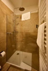 Eine moderne Dusche mit Glaswand und warmen Fliesen. Handtücher und Toilettenpapier sind gut sichtbar.
