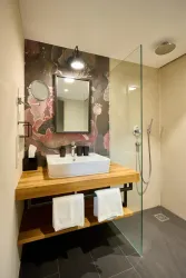 Ein modernes Badezimmer mit einem Holzwaschtisch und einer Glasdusche. Die Wand ist mit einem kunstvollen, floralem Muster dekoriert.