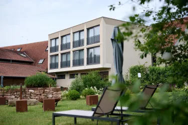 Ein modernes Hotelgebäude mit mehreren Fenstern und Balkonen. Im Vordergrund sind Liegen und eine grüne Wiese zu sehen.