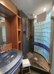 Ein modernes Badezimmer mit einer freistehenden Dusche und blauen Glasbausteinen. Der Waschplatz ist aus dunklem Material und es gibt Holzregale.