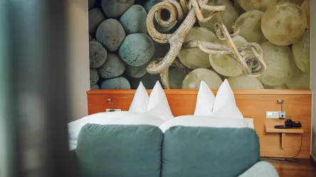 Ein gemütliches Schlafzimmer mit einem großen Bett und zwei Kissen. Im Hintergrund ist eine dekorative Wand mit blauen und grünen Trauben auf Fototapete.