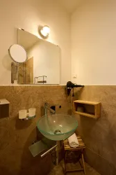 Ein modernes Badezimmer mit einem runden Glaswaschtisch und einem großen Spiegel. An der Wand befindet sich ein kleiner Holzregal und ein Handtuchhalter.