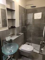 Ein modernes Badezimmer mit einer Glasdusche und einem Waschbecken aus Glas. Die Wände sind in neutralen Grautönen gefliest.