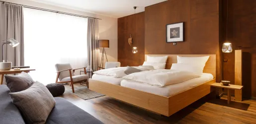 Ein modernes Hotelzimmer mit einem komfortablen Doppelbett und eleganten Möbeln. Große Fenster sorgen für viel Tageslicht.