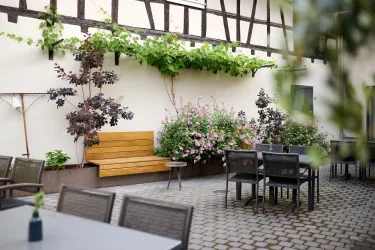 Ein einladender Innenhof mit einer Holzbank und blühenden Pflanzen. Tische und Stühle laden zum Verweilen ein.