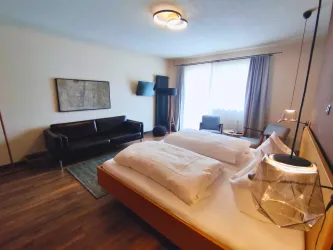 Ein modernes Hotelzimmer mit zwei Betten und einem gemütlichen Sofa. Große Fenster sorgen für viel Tageslicht.