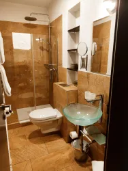 Ein modernes Badezimmer mit einer Dusche aus Glas und einer klaren Glaswaschtisch. Die Wände sind mit hellen Fliesen verkleidet und es gibt eine große Spiegeloberfläche.