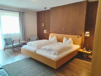 Ein modernes Schlafzimmer mit zwei Betten und weißen Bettdecken. Der Raum ist hell und gemütlich, mit einem Tisch und Stühlen neben dem Fenster.