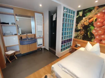 Ein modernes Hotelzimmer mit einem Einzelbett und einer offenen Badezimmernische. Die Wände sind mit einer lebendigen Fototapeten gestaltet.