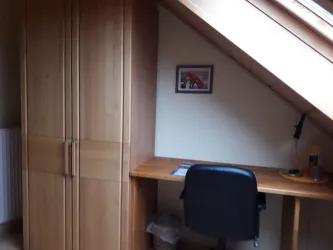 Ein gemütliches Arbeitszimmer mit einem Schreibtisch und einem Stuhl. An der Wand hängt ein Bild, und es gibt einen großen Holzschrank.