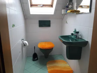 Ein kleines Badezimmer mit einem Fenster und modernen Sanitäranlagen. Der Boden ist mit bunten Teppichen in Orange und Blau dekoriert.